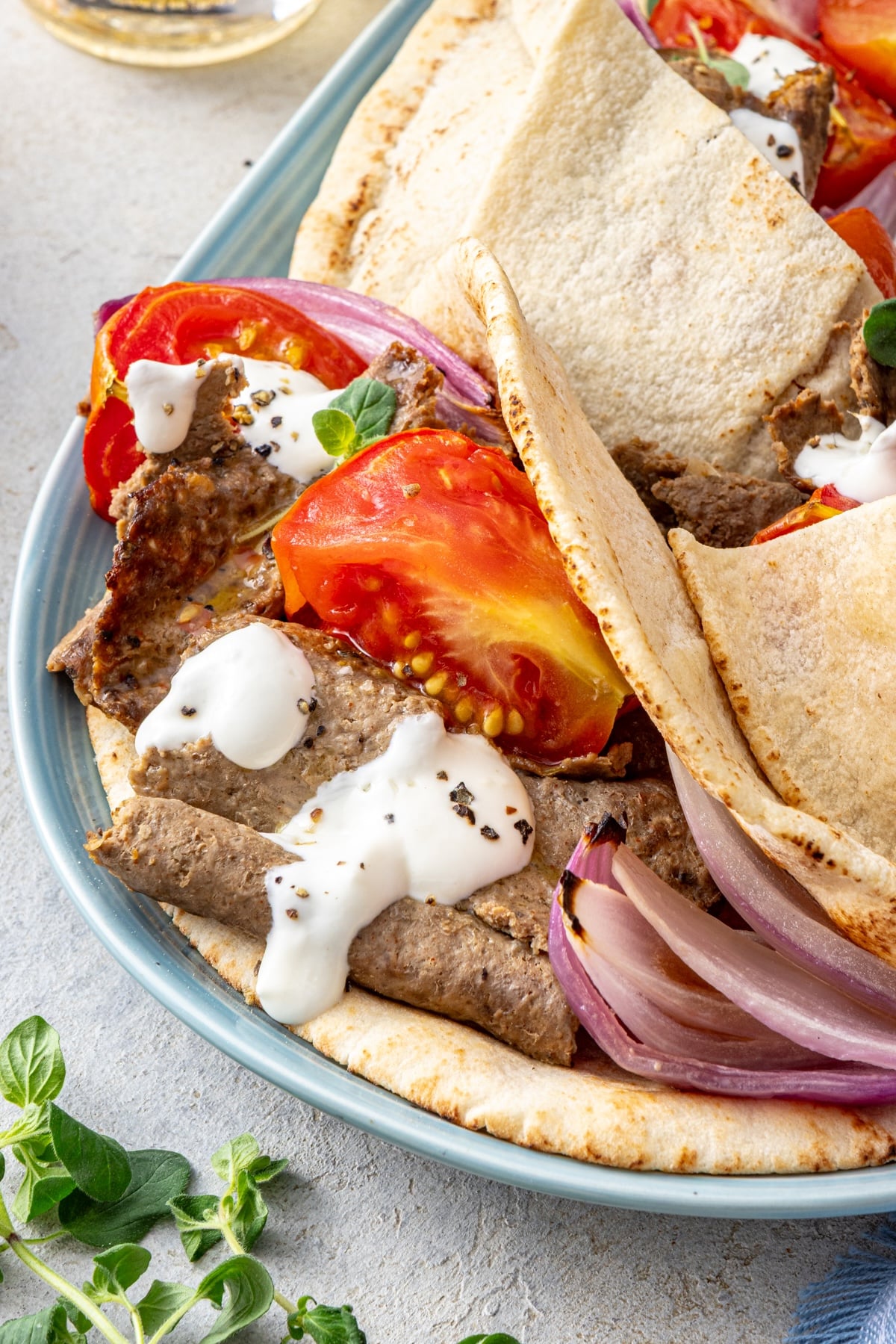 Homemade doner kebab stuffed inside warm pita pockets with roasted tomatoes, red onion, and yogurt sauce on a blue platter.