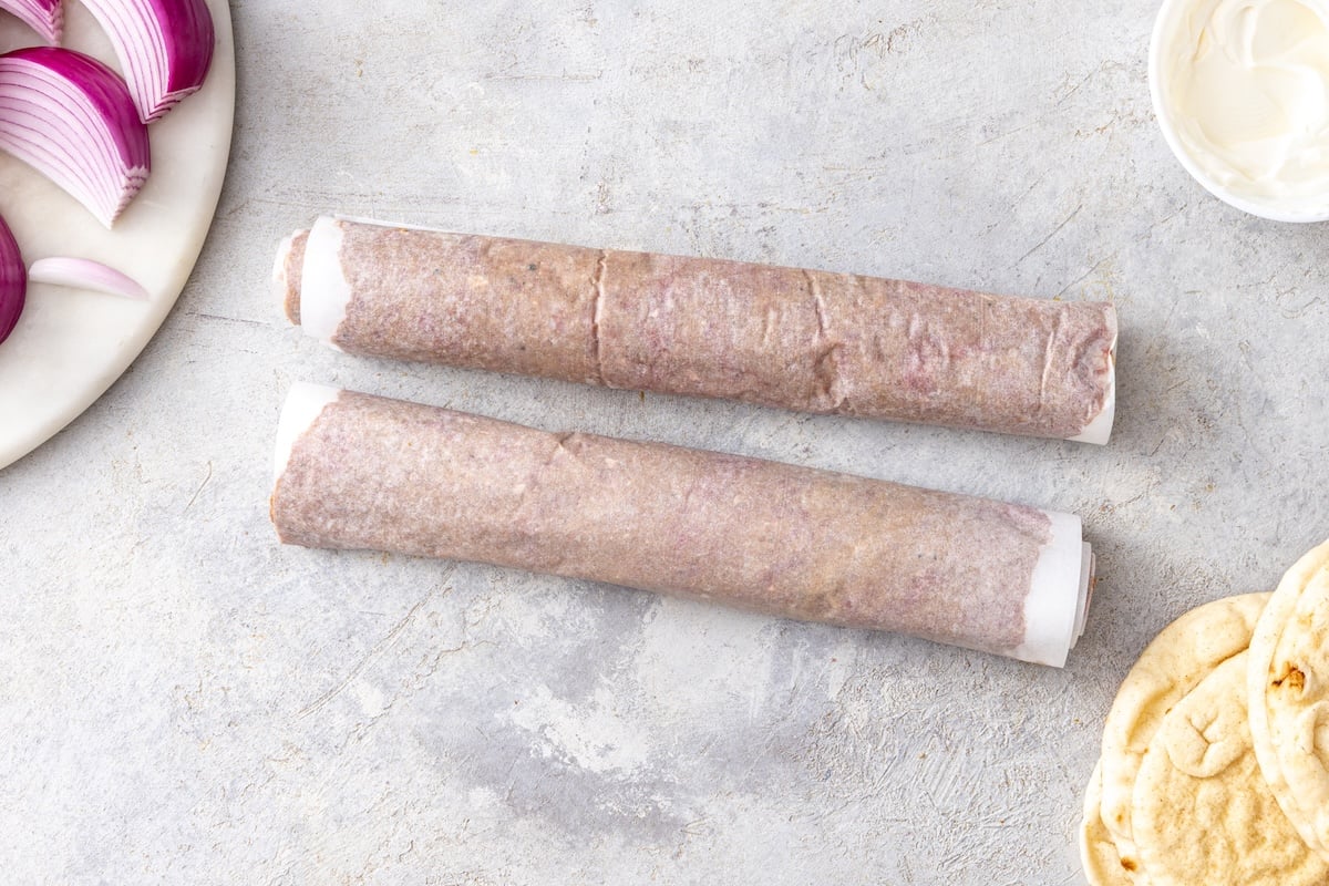 Two ground beef doner kebab cylinders rolled tightly in parchment paper ready to bake.