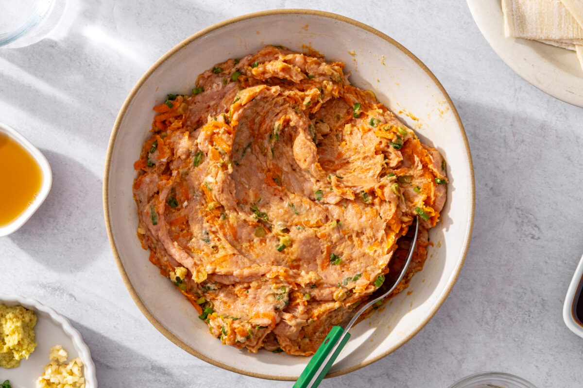 Ground meat filling mixed with grated carrot, scallions, ginger, and garlic in a bowl.