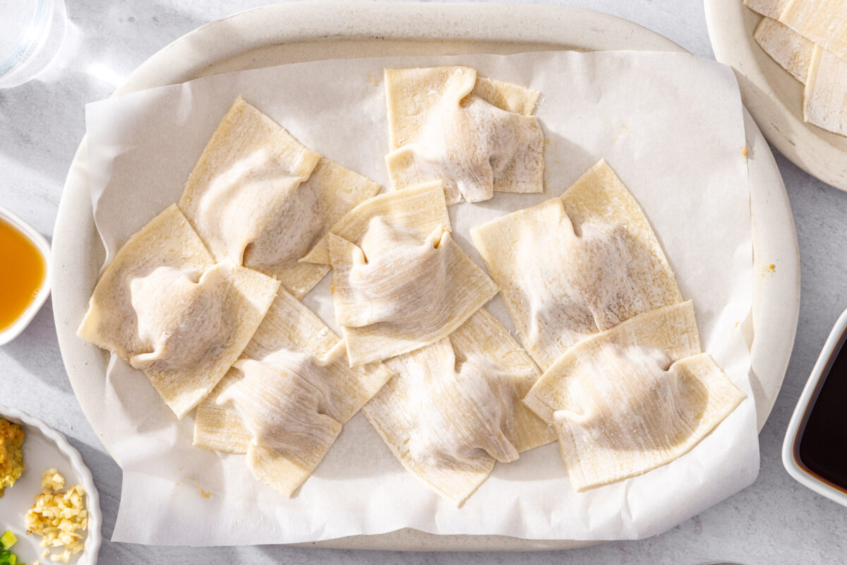 Dumpling wrappers draped over meatballs on a parchment-lined plate before cooking.